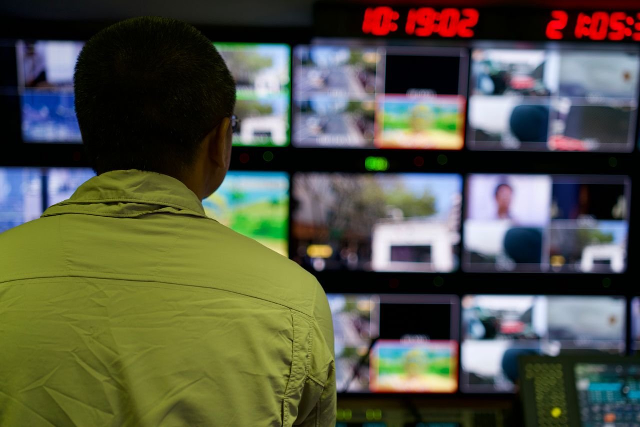 our-story-01 Man in a control room overseeing multiple monitors displaying various scenes.